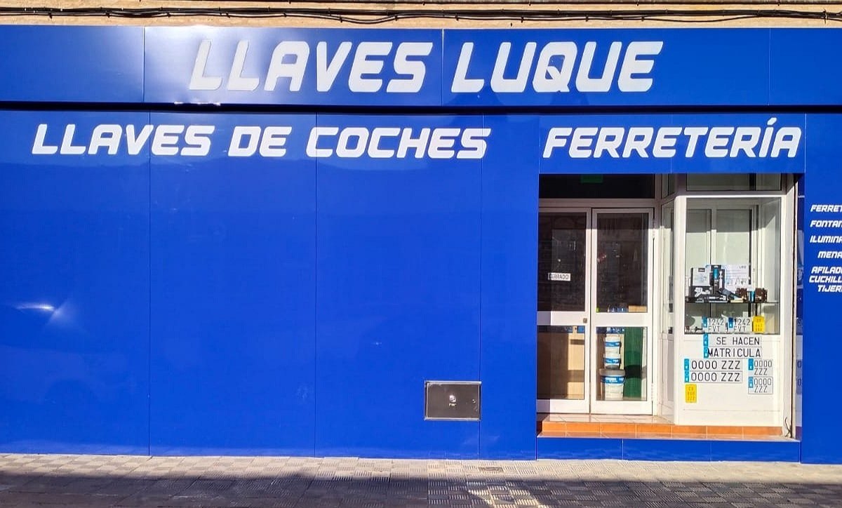Fachada azul de Llaves Luque con letras blancas: llaves de coches y ferretería, y un escaparate con matrículas de muestra