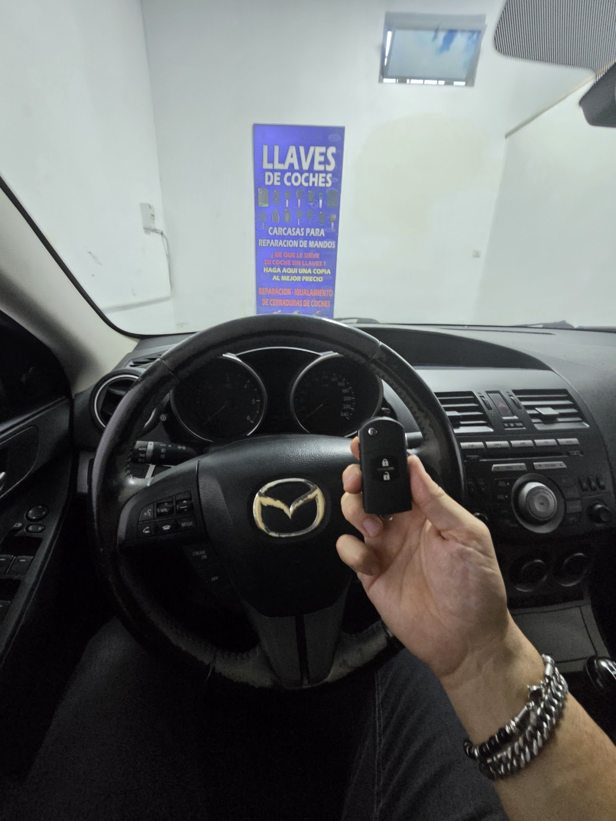 Mano con una llave de mando dentro de un coche, frente al cartel de llaves de coches